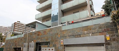 Een meerlaags gebouw met een modern ontwerp, met een combinatie van glazen en metalen balkonnes, een zichtbare ingang en een gesloten garagepoort.