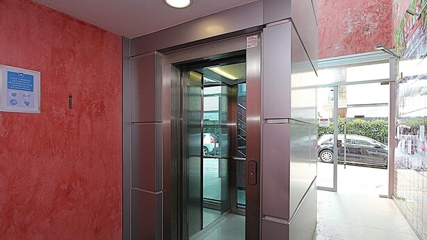 An elevator entrance with a glass door, a metal frame, and a sign on the wall. - Cozy Apartment with A/C, 150m from Lloret de Mar Beach (Lloret de Mar)