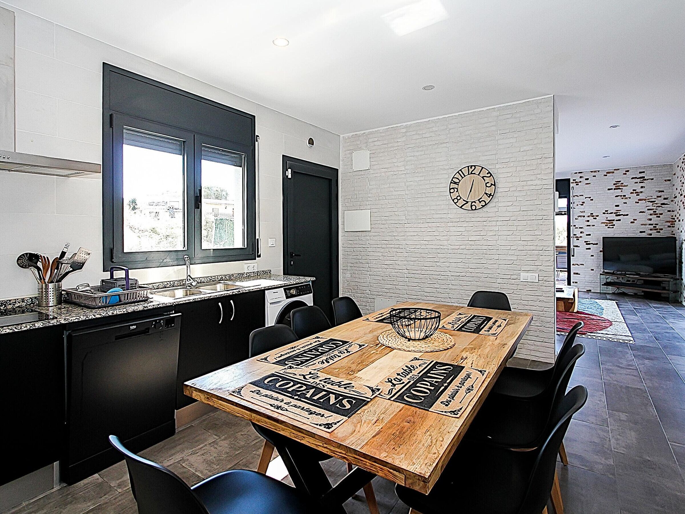 Una cocina moderna con comedor, que incluye una mesa de madera con estampado de periódico antiguo, sillas negras y una pared con diseño de ladrillo.