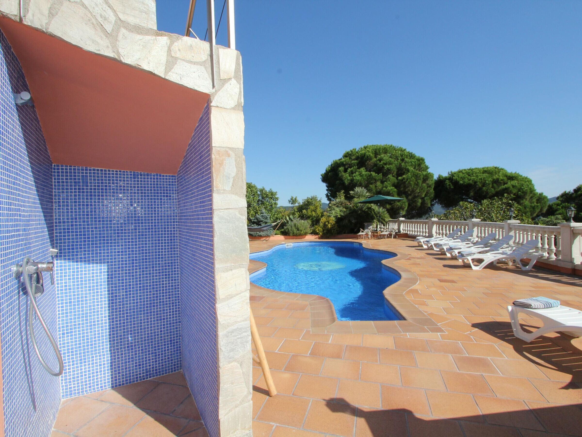 Una piscina con borde de azulejos, zona de duchas separada y sillones de descanso alrededor.