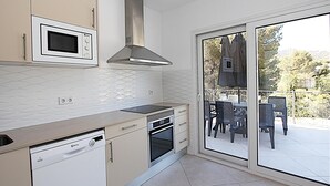 Cozinha moderna equipada com micro-ondas, forno e máquina de lavar loiça, com acesso a um alpendre com área de estar ao ar livre.