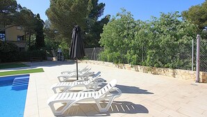 Uma área à beira da piscina com espreguiçadeiras e um guarda-sol, cercada por um muro de pedra e vegetação.