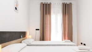 Hotellihuone, jossa on kaksi sänkyä, yöpöytä lampulla, pistorasia ja ikkuna, jossa on verhot.