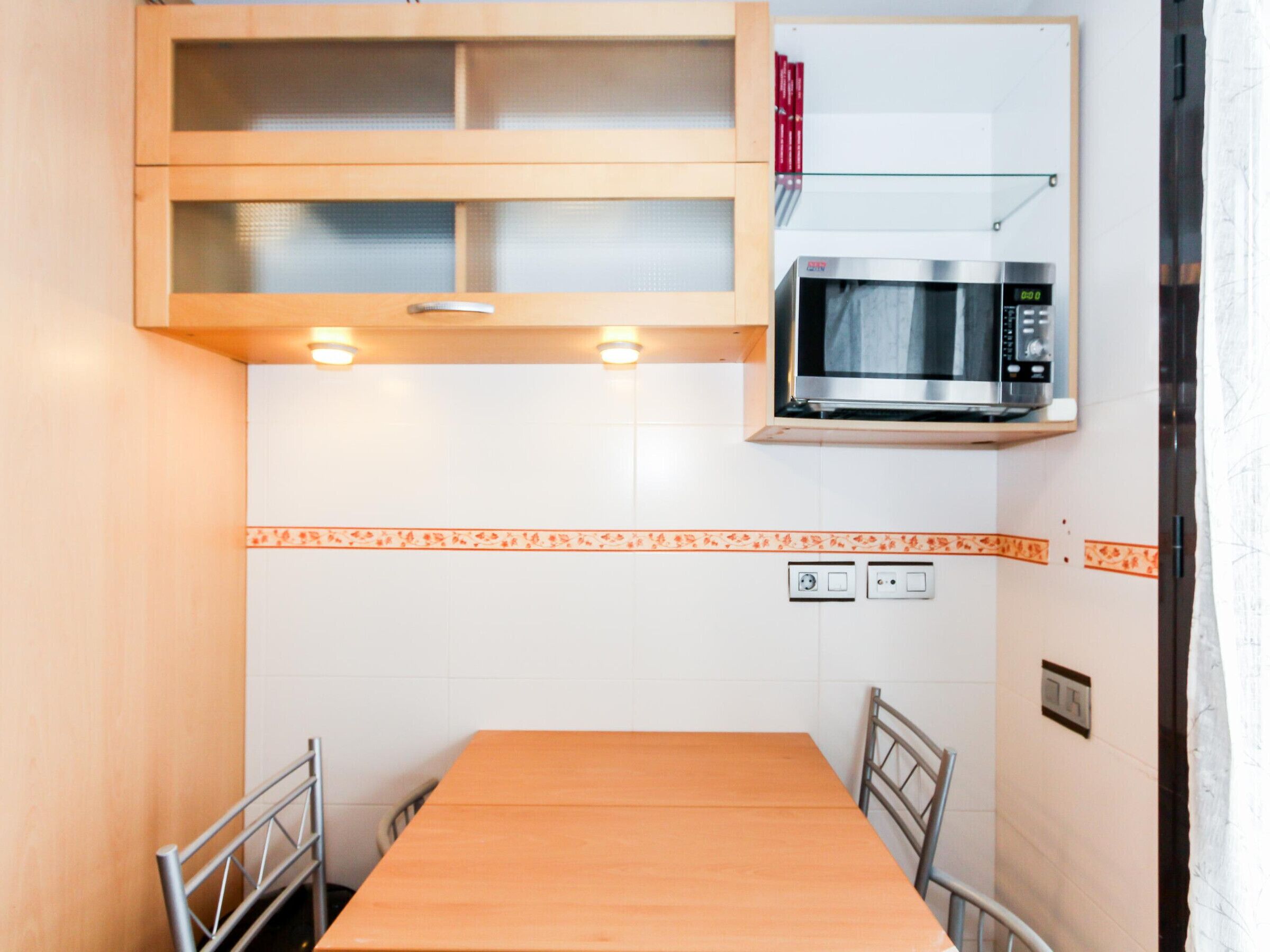 A compact kitchen with a wooden table, two chairs, a microwave, and a shelf above the counter.