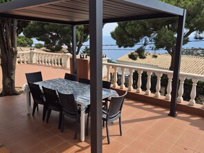 Un patio exterior con una mesa y sillas, una pérgola y vista al mar.
