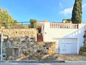 Una casa de dos pisos con un muro de piedra, un garaje blanco y una escalera que conduce al piso superior.