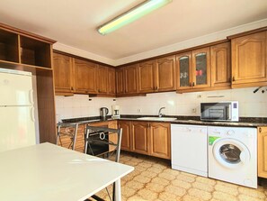 Una cocina con armarios de madera, un refrigerador blanco, un microondas, un lavamanos y una lavadora.
