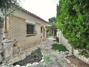A house with a brick exterior, stone pathway, and a garden with various plants and a small tree. - Modern villa 1 km from beach with private pool and sea views (Lloret de Mar)