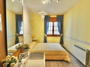 A hotel room with a bed, a sink, a mirror, a window with curtains, and a radiator. - Modern villa 1 km from beach with private pool and sea views (Lloret de Mar)