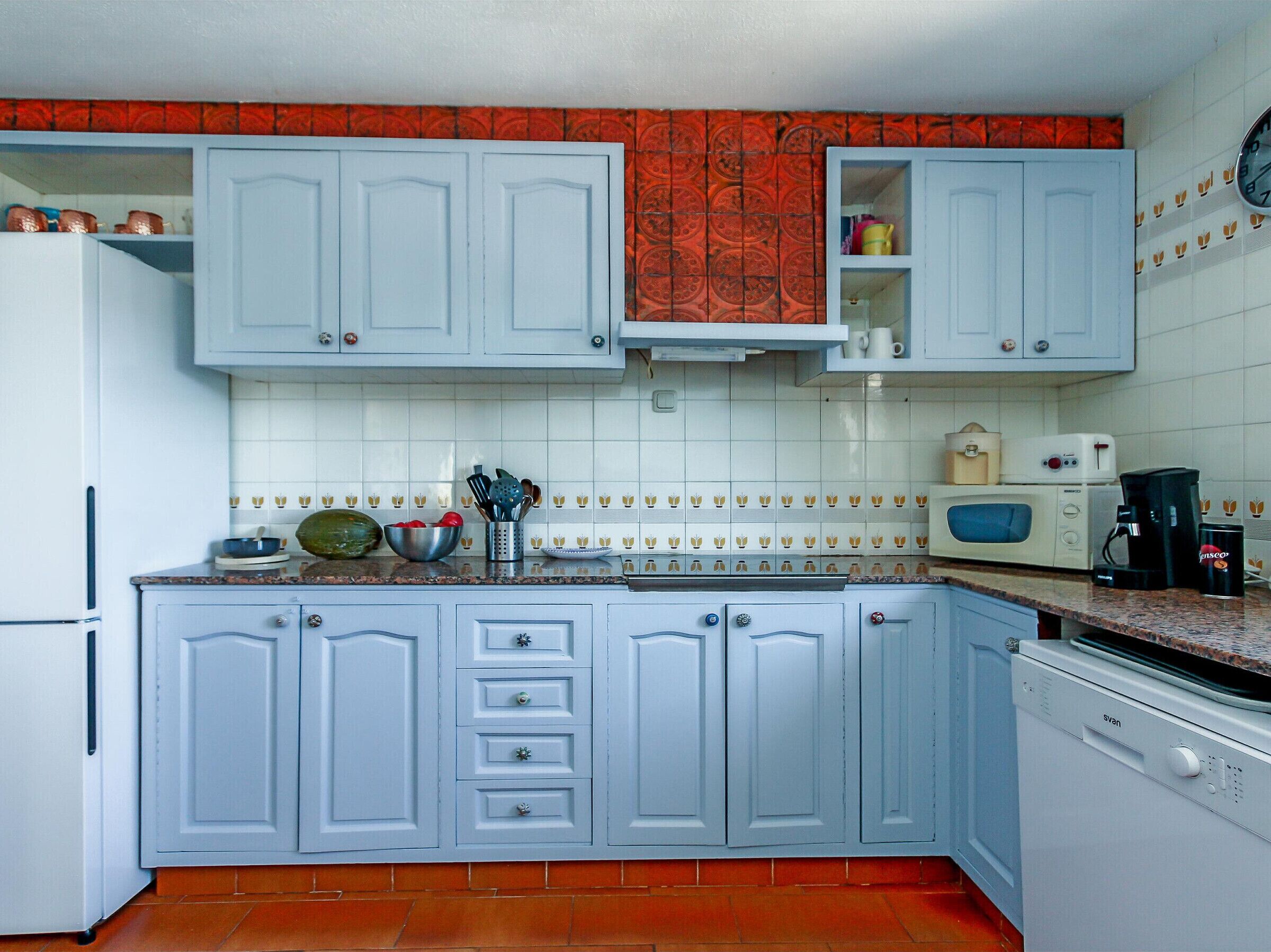 Una cocina con armarios azul claro, microondas, cafetera y lavavajillas.