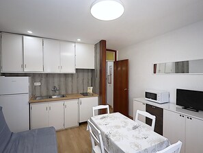 Cocina compacta con armarios blancos, microondas, refrigerador pequeño y comedor con mesa y sillas.