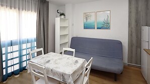 Ein Zimmer mit Esstisch, Stühlen, einer Couch, einem weißen Regal und zwei Wandbildern.