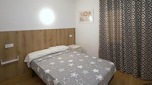Ein Schlafzimmer mit einem Bett, einem Nachttisch, einer Steckdose und einem gemusterten Vorhang.