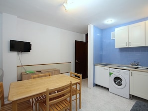 Eine kompakte Küche mit Waschmaschine, einem Esstisch mit Stühlen und einem an der Wand befestigten Fernseher.