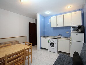 A compact kitchen with a washing machine, a microwave, and a refrigerator. There is a wooden dining table and chairs.