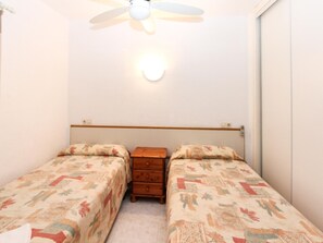 A small, single-room bedroom with two single beds, a wooden nightstand, a ceiling fan, and a wall-mounted light. - Apartment in Lloret Center, 2-4 People, Close to the Sea (Lloret de Mar)