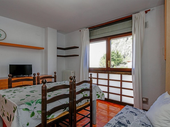 A bedroom with a bed, a chair, a table with a television, and a window with curtains.