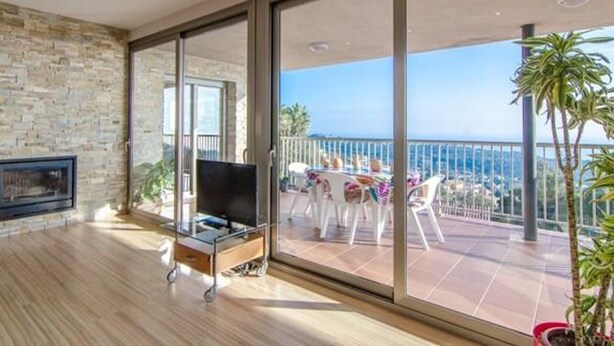 Ein modernes Wohnzimmer mit Steinwand, einem Fernseher auf einem Glastisch und einem Balkon mit Meerblick.