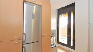 Een compacte keuken met een roestvrijstalen koelkast, houten kastjes en een schuifdeur naar een balkon.