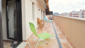 Een balkon met een betegelde vloer, een schuifdeur van glas en twee groene lounge stoelen.