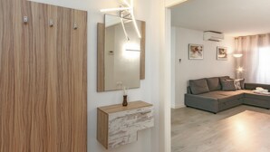 A modern living room with a wooden accent wall, a large mirror, and a grey sectional sofa. - Cozy New Apartment, Beach 150m, Internet, A/C, Pool Access, Lloret de Mar (Lloret de Mar)