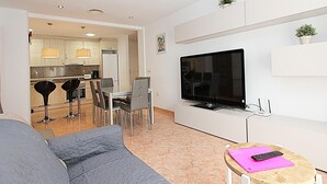 Ein modernes Wohnzimmer mit einem grauen Sofa, einem an der Wand montierten Fernseher und einem kleinen Holztisch mit einer Fernbedienung.