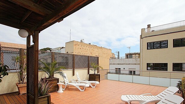 Eine Dachterrasse mit Holzboden, weißen Lounge-Sesseln und Topfpflanzen.