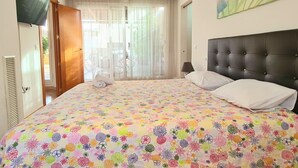 Ein Schlafzimmer mit einem großen Bett, einem an der Wand montierten Fernseher und einem Fenster mit transparenten Vorhängen.