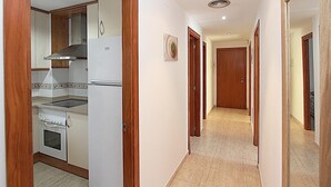Ein Korridor mit Küchenzeile links, ausgestattet mit Kühlschrank, Backofen und Herd. Der Korridor besitzt Holztüren und geflieste Böden.