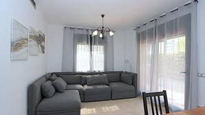 Ein modernes Wohnzimmer mit einem grauen Ecksofa, einem Holzessttisch und einer Chandelüster.