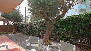 Ein Sitzbereich im Freien mit zwei Metallstühlen und einem kleinen Tisch, umgeben von Kies und einer Hecke.