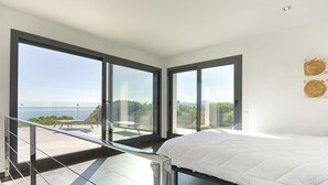 Une chambre moderne avec un grand lit, un balcon doté d’une porte vitrée et une vue sur la mer.