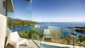 Un balcon moderne doté d’une barrière en verre, d’une piscine et offrant une vue sur la mer et les collines.
