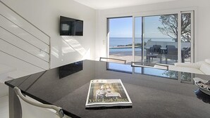 Une cuisine moderne dotée d’un grand îlot central, d’un magazine posé sur le plan de travail et offrant une vue sur la mer grâce à de grandes portes coulissantes.
