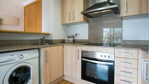 A compact kitchen with a washing machine, oven, and stainless steel range hood. - Charming Family Apartment in Santa Margarita: Pool, Parking, Near Beach and Shops (Roses)