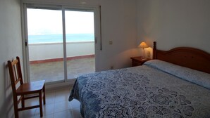 A bedroom with a bed, a chair, a nightstand, and a view of the sea through a sliding door. - Seafront Penthouse for 6 with Terrace and Shared Pool (El Port de la Selva)