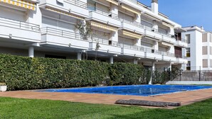 A multi-story residential building with balconies, a swimming pool, and a well-maintained garden. - Seafront Penthouse for 6 with Terrace and Shared Pool (El Port de la Selva)
