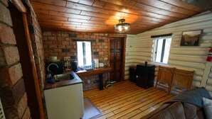 A log cabin interior with a kitchen area, wooden floors, a couch, and a fireplace. - Wildlife Lookout Summ (Mount Laguna)