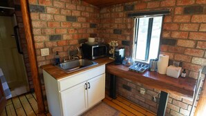 A compact kitchen with wooden flooring, a brick wall, and a window. - Wildlife Lookout Summ (Mount Laguna)