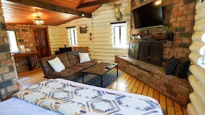 A log cabin interior with a bed, sofa, fireplace, TV, and wooden floors. - Wildlife Lookout Summ (Mount Laguna)