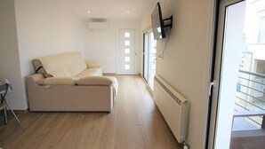 A modern living room with a sofa, a TV mounted on the wall, and a sliding glass door leading to an outdoor balcony. - Modern Renovated 3BR Apartment, 50m from Beach, Heart of Llançà Port (Llançà)