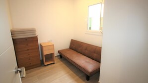 A small, well-lit room with a wooden dresser, a small nightstand with drawers, a bench, and a window with blinds. - Modern Renovated 3BR Apartment, 50m from Beach, Heart of Llançà Port (Llançà)