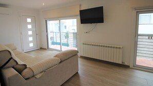A modern living room with a sofa, a flat-screen TV, and a sliding glass door leading to a balcony. - Modern Renovated 3BR Apartment, 50m from Beach, Heart of Llançà Port (Llançà)