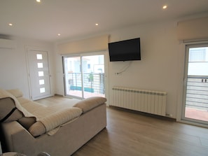 Ein modernes Wohnzimmer mit einer Couch, einem Flachbildfernseher und einer Glastür, die auf einen Balkon führt.