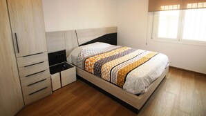 A bedroom with a wooden bed frame, a nightstand, a wardrobe, and a window with blinds. - Modern Renovated 3BR Apartment, 50m from Beach, Heart of Llançà Port (Llançà)