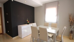 A modern dining area with a white table and chairs, a black accent wall, and a window with curtains.