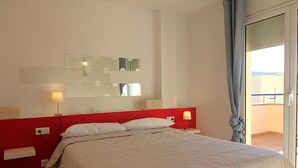 A hotel room with a bed, a red headboard, a large mirror, and a view of the outside.