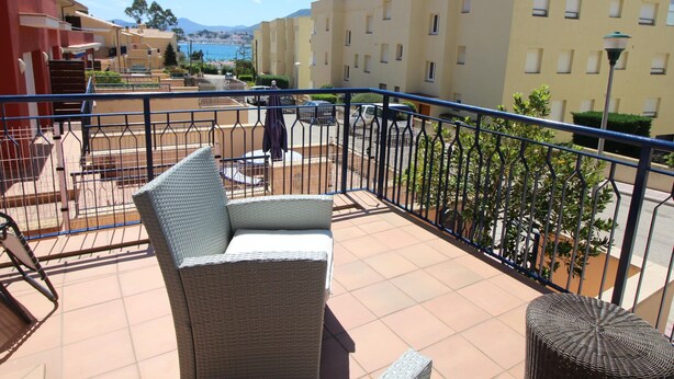 A balcony with wicker furniture, a view of a coastal town, and buildings in the background.