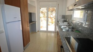 A kitchen with a white refrigerator, wooden cabinets, granite countertops, a stainless steel sink, and a window overlooking a stone wall.