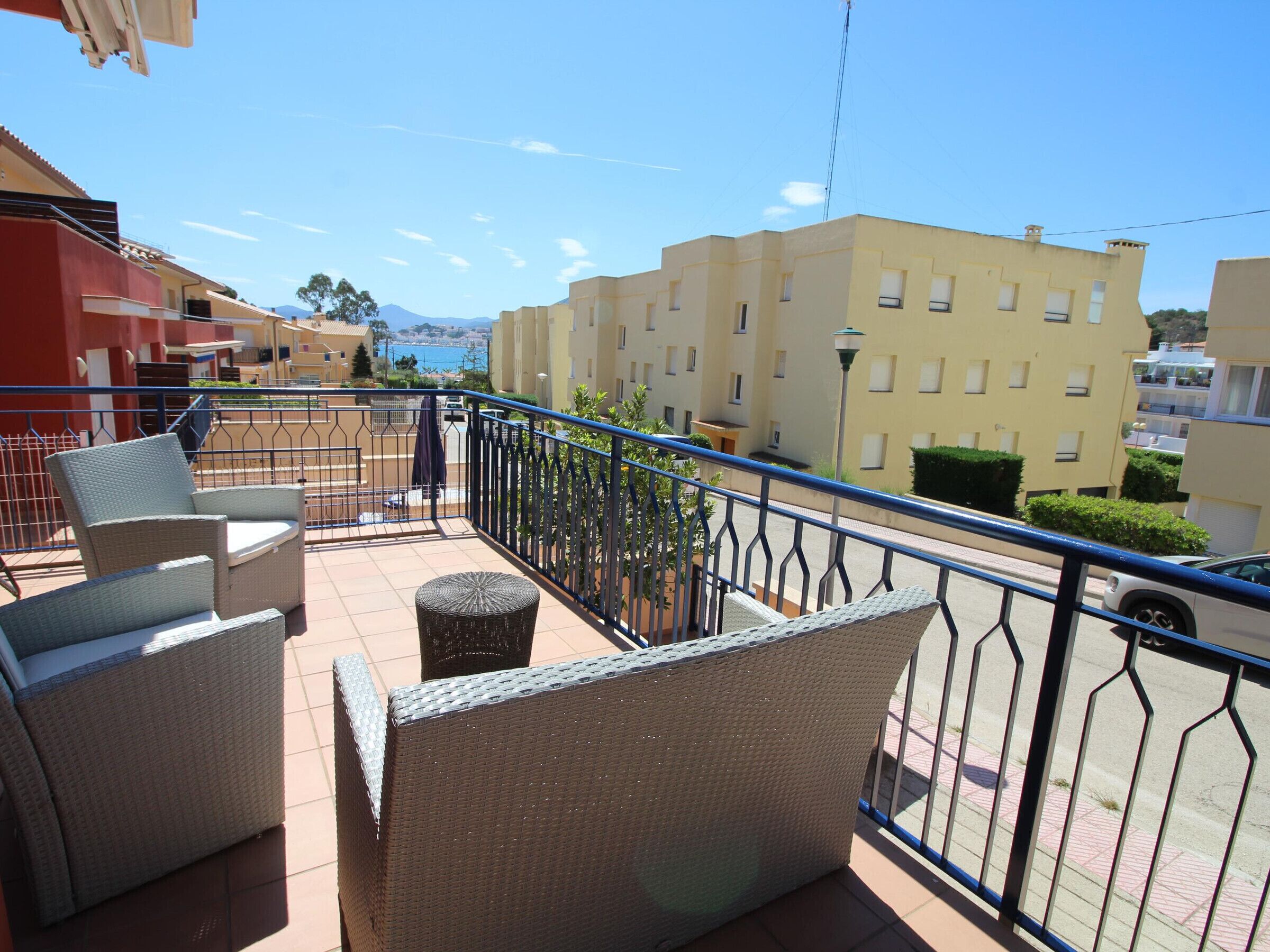 A balcony with wicker furniture, a view of a yellow building, and a clear sky.
